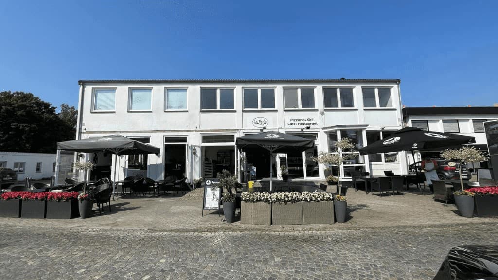 Die Fassade des Restaurant La Perla mit großen schwarzen Tischen und Sonnenschirmen